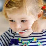 Kleines Mädchen beim Essen, mit zwei Zöpfen und gestreiftem Oberteil